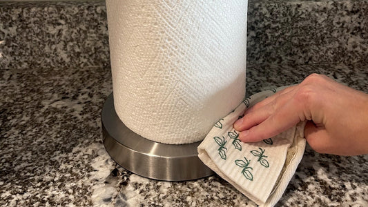 Wiping a kitchen counter with a Swedish dishcloth next to a paper towel holder
