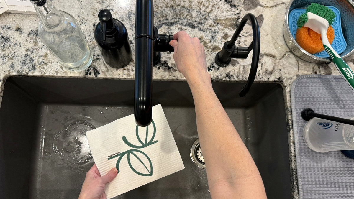 Hands rinsing a Swedish dishcloth under a kitchen faucet at the sink