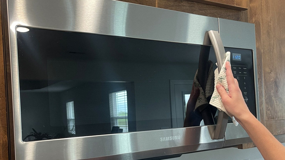 Hand wiping a stainless steel microwave handle with a Swedish dishcloth
