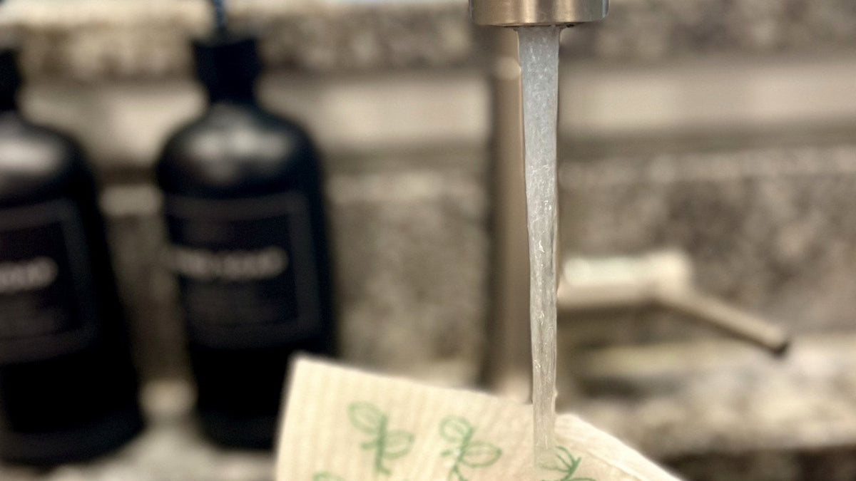 Hand rinsing a Swedish dishcloth under a kitchen faucet after a vinegar soak