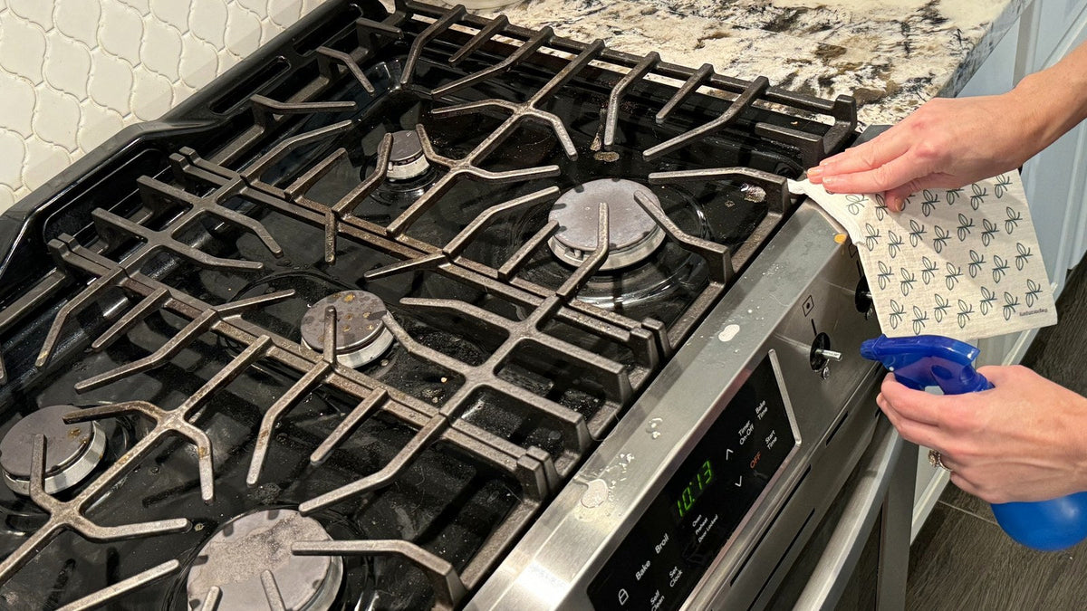 Hand spraying a gas stovetop and wiping it with a Swedish dishcloth instead of paper towels