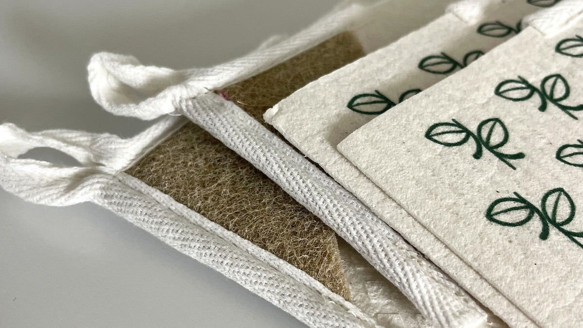 Stack of Giro Swedish dishcloths showing white cotton hang loops, tan sisal scouring corners, and a green leaf print