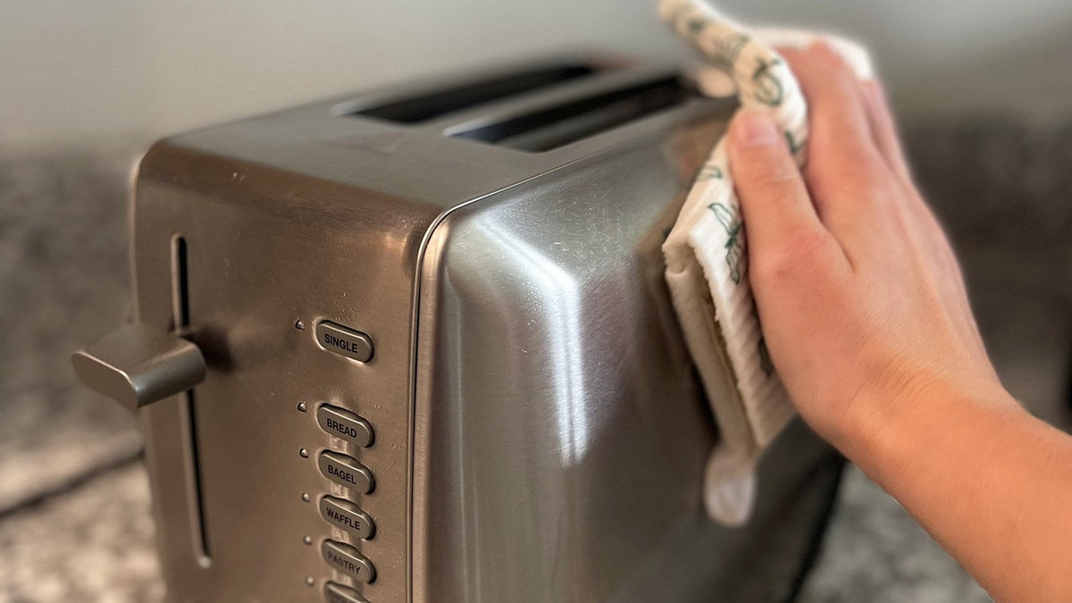 Hand wiping the side of a stainless steel toaster with a Giro Swedish dishcloth on a granite counter