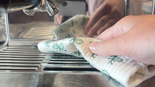 Hand wiping the stainless steel drip tray grate of an espresso machine with a leaf-print Giro Swedish dishcloth