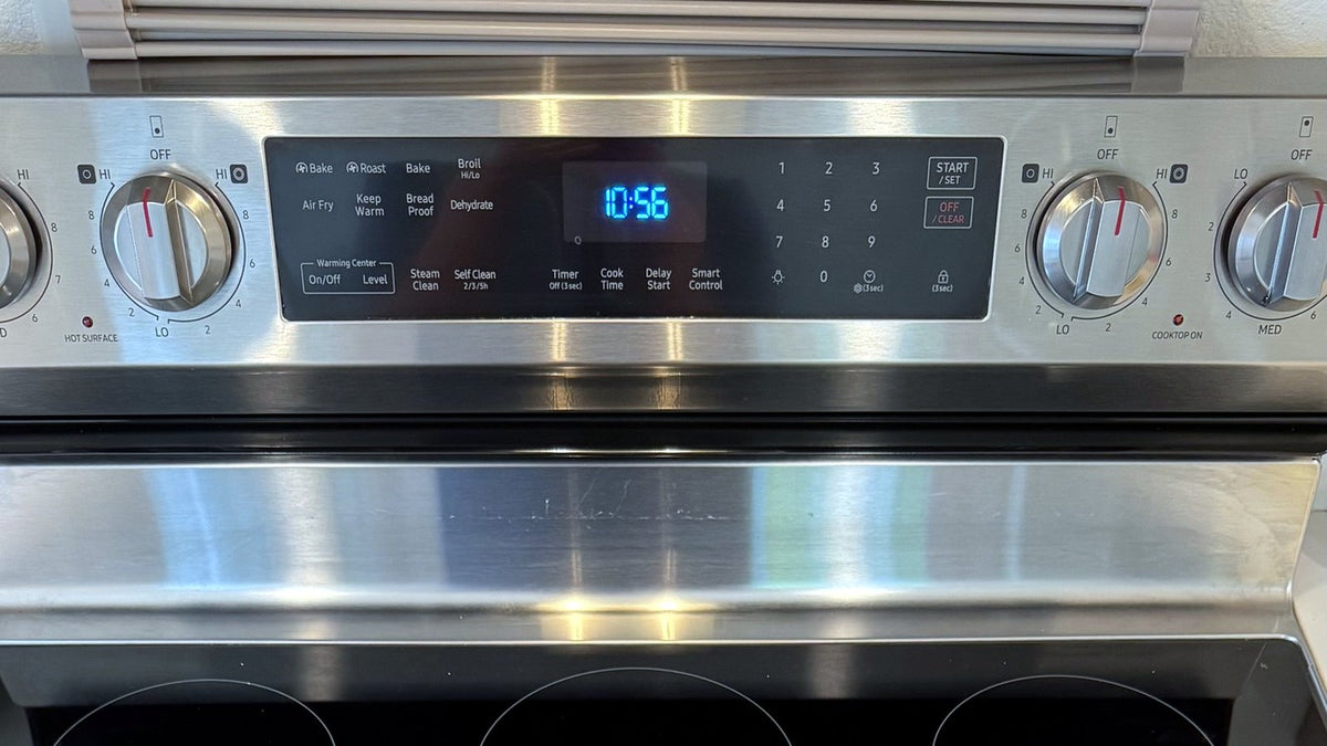 Stainless steel range control panel with Self Clean and Steam Clean buttons, oven knobs, and a digital clock above a glass cooktop
