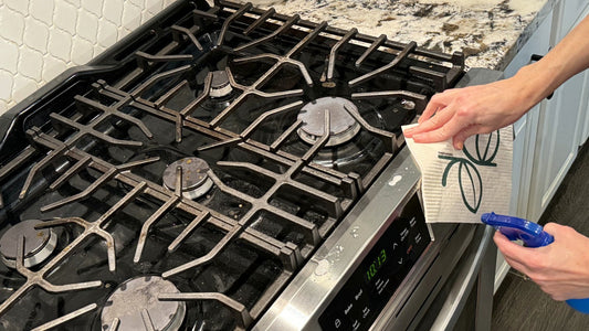Hand wiping the edge of a gas stove top with a Giro Swedish dishcloth, cast iron grates and burner caps in view