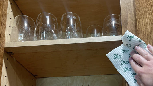 Wiping out a kitchen cabinet shelf of glassware with a Swedish dishcloth