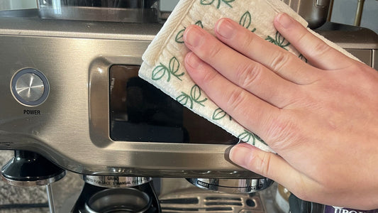 Hand wiping an espresso machine with a Swedish dishcloth