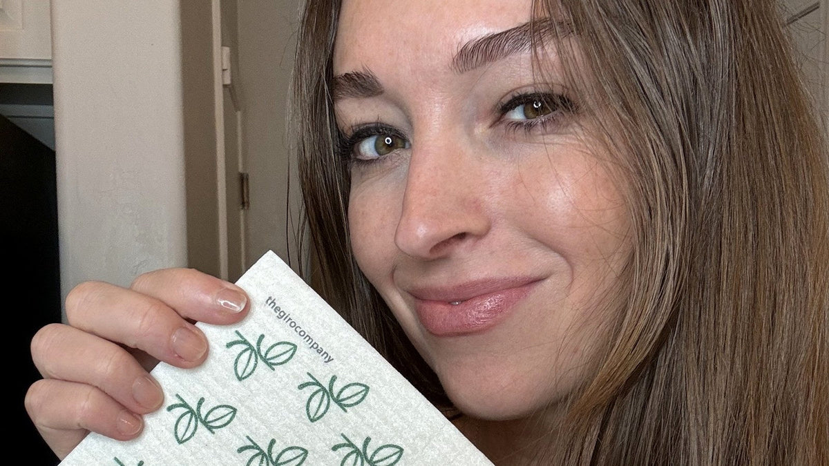 Smiling woman holding up a leaf-print Giro Swedish dishcloth, a plastic-free stocking stuffer